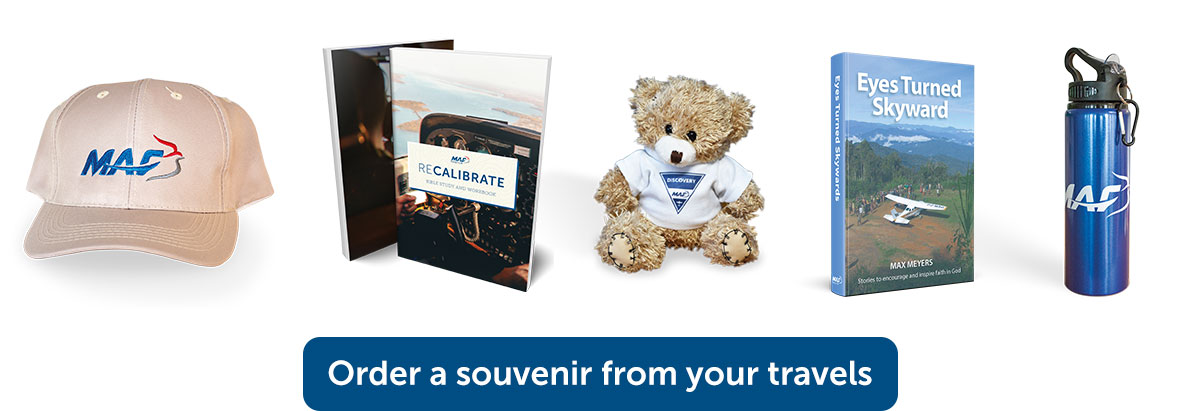Selection of discovery souvenirs: Cap, Recalibrate book, Toy bear, Eyes turned skyward book and MAF water bottle with caption 